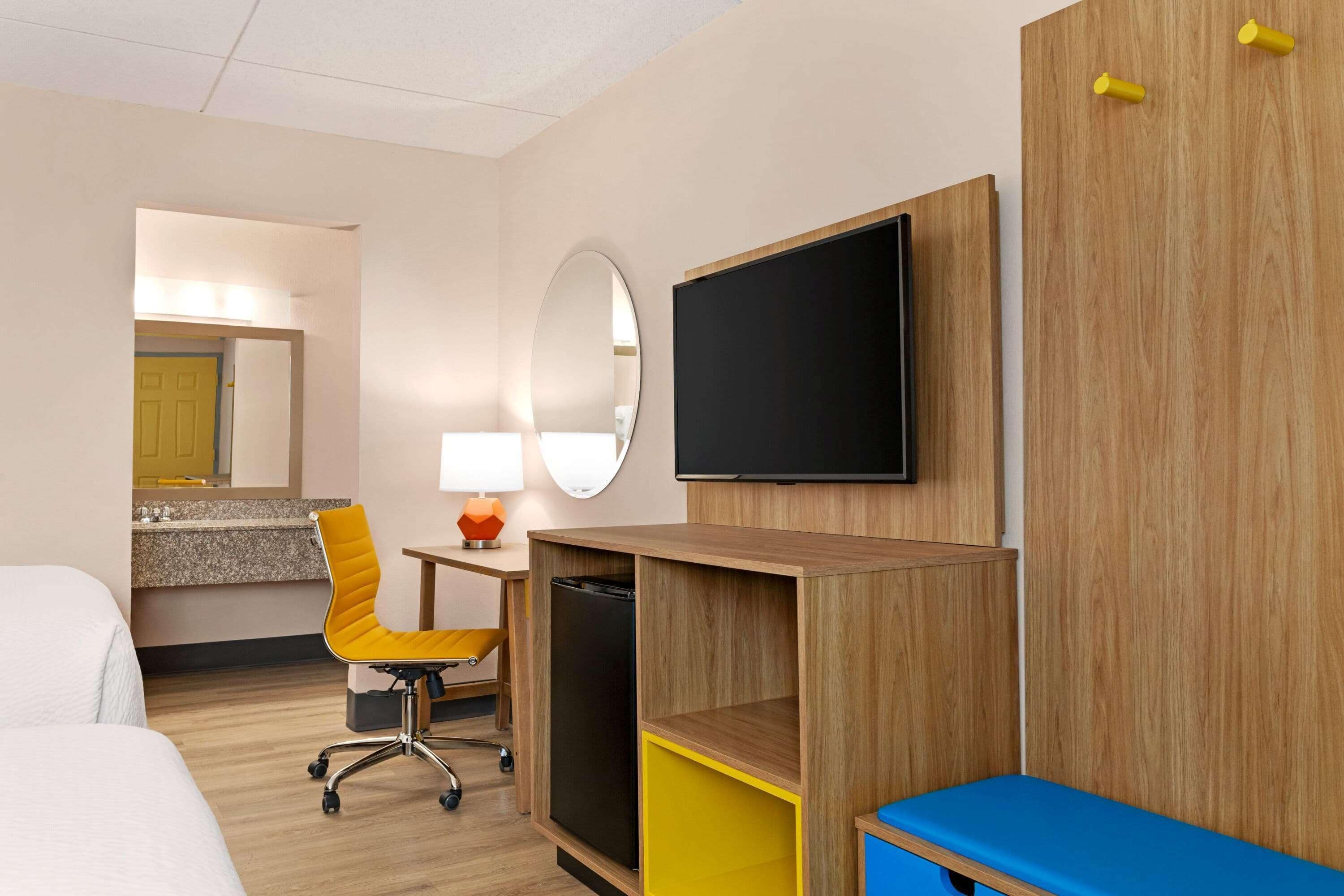 A hotel room with a bed, a desk with a computer, a chair, a TV, and a mirror.
