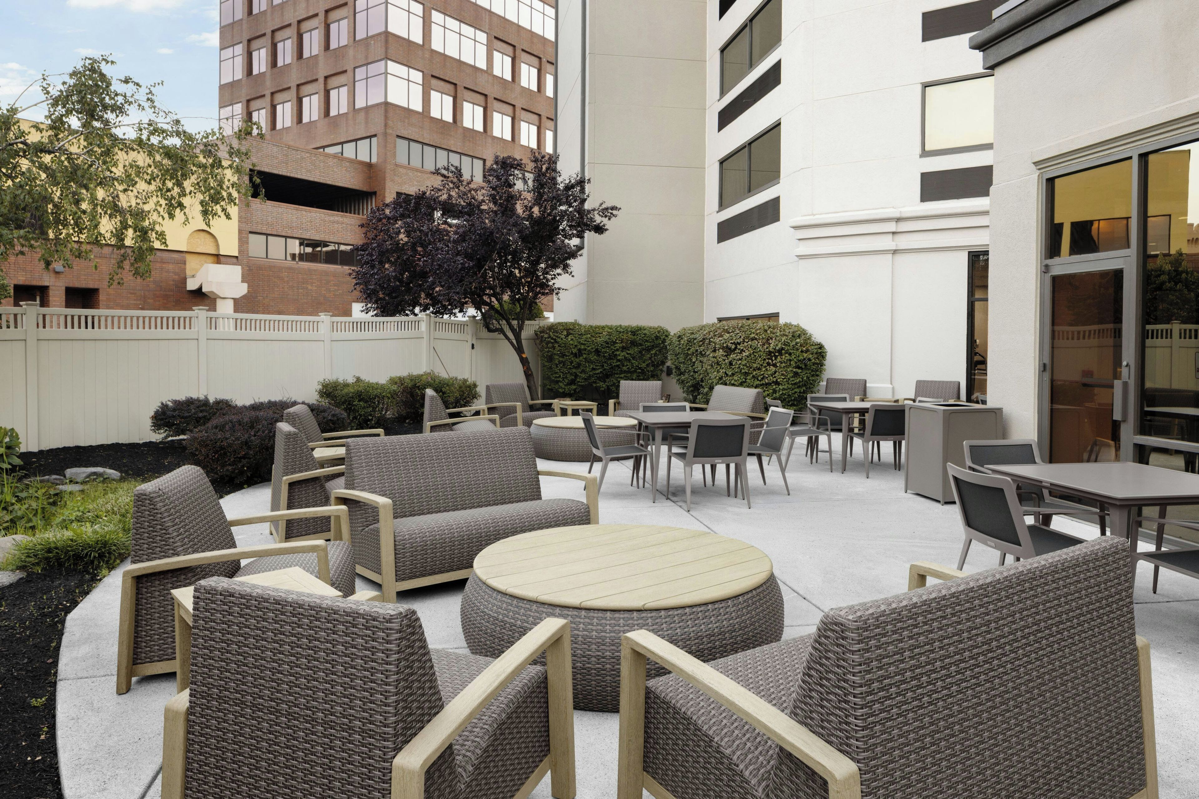Un espace extérieur aménagé en terrasse, avec des meubles en osier, notamment des canapés et des tables, entouré d’une petite clôture blanche et de verdure.