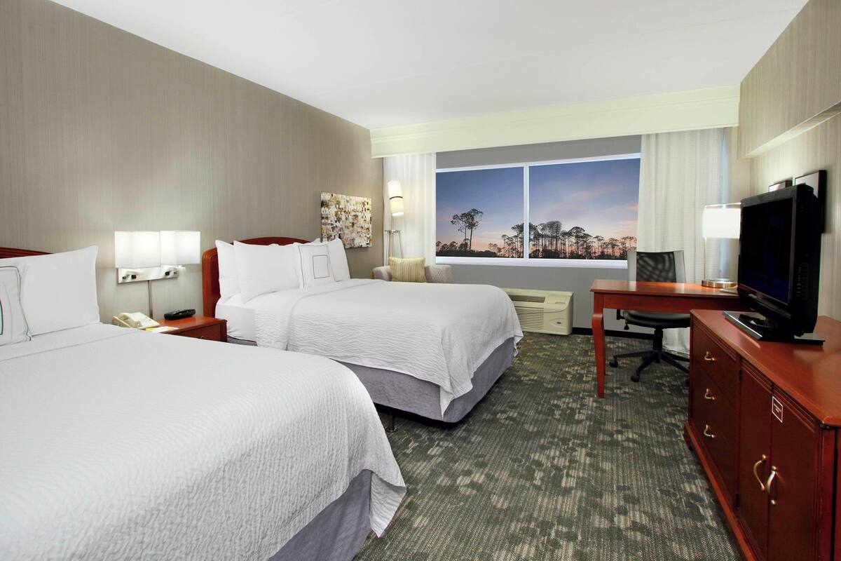 Habitación de hotel con dos camas, un escritorio, televisión y ventana con vistas a la ciudad.