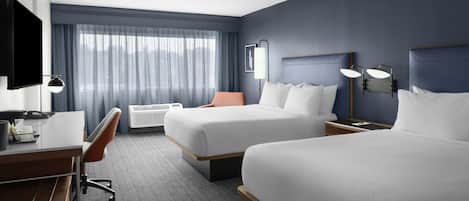Ein Hotelzimmer mit zwei Betten, einem Schreibtisch, einem Stuhl, einem Fernseher und einem Fenster mit Vorhängen.