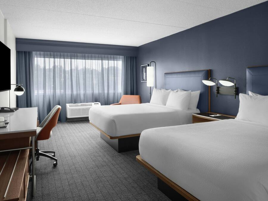 A hotel room with two beds, a desk, a chair, a TV, and a window with curtains.