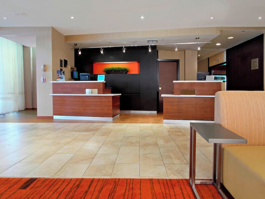 Zona de recepción de hotel con diseño moderno, que incluye un mostrador de recepción, un área de descanso y un amplio ventanal que proporciona luz natural.