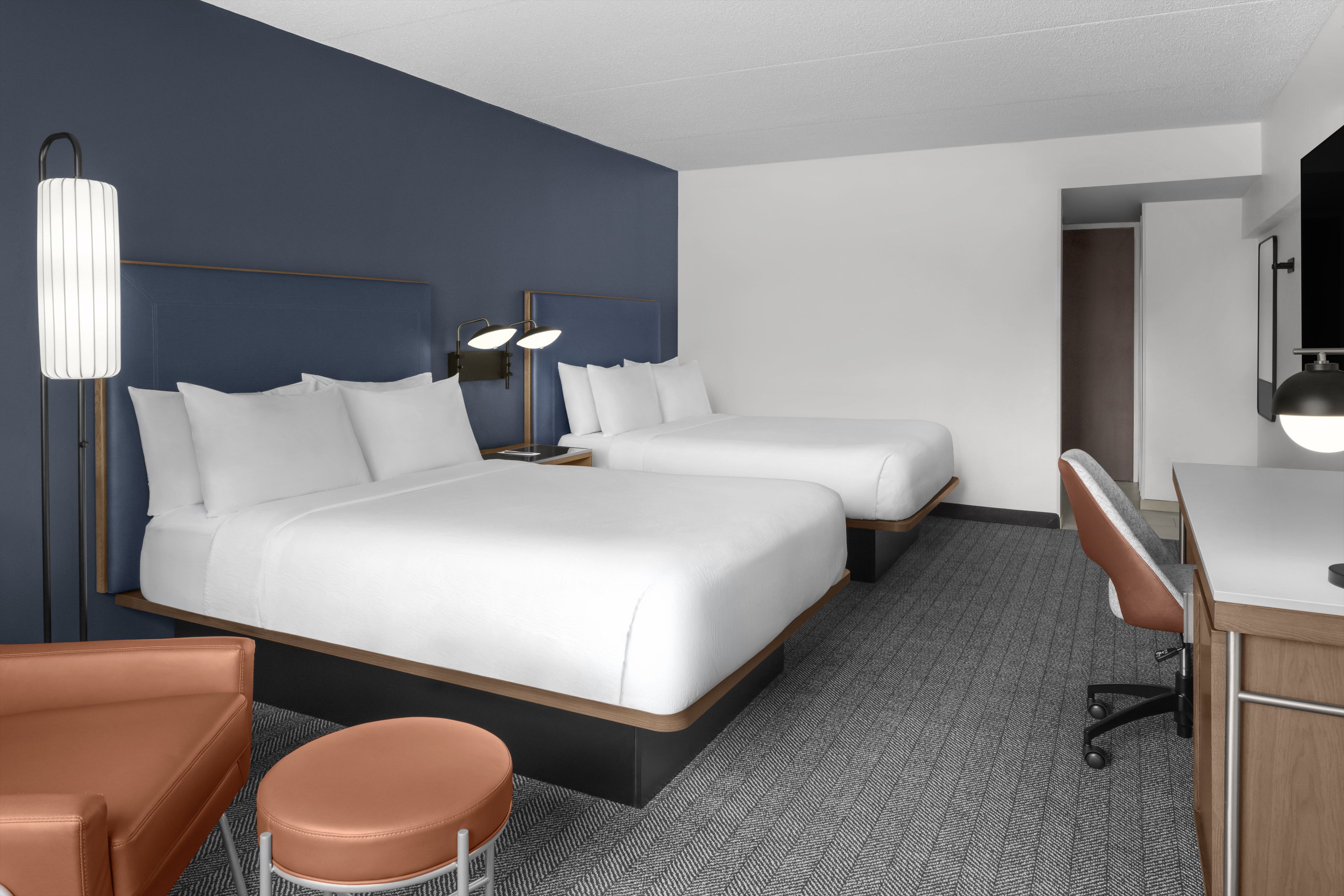 A hotel room with two beds, a desk, a chair, and a large mirror.