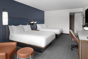 Ein Hotelzimmer mit zwei Betten, einem Schreibtisch, einem Stuhl und einem großen Spiegel.