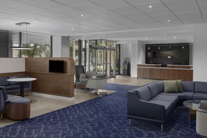 En moderne lobby med siddeområder, en receptionsdisk og et stort skærmbillede.