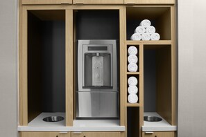 Une cuisine équipée d’un réfrigérateur en acier inoxydable encastré, de deux éviers et d’une étagère où sont rangées des serviettes enroulées.