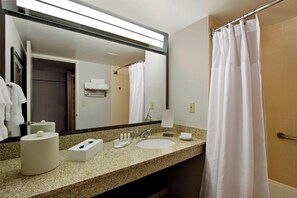 Une salle de bain d’hôtel équipée d’un lavabo, d’un miroir, d’un porte-serviettes et d’un rideau de douche.