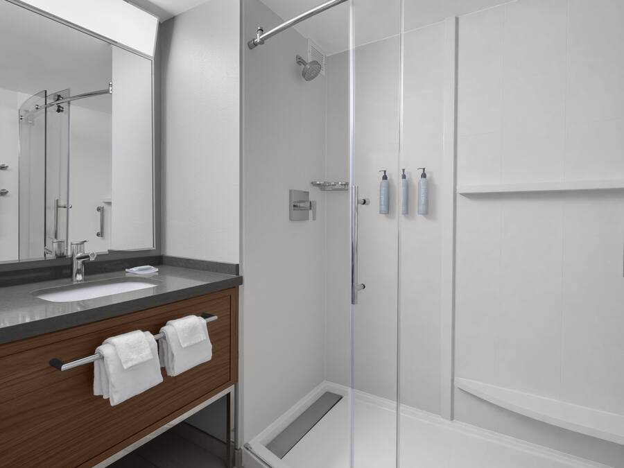 A modern bathroom with a glass shower enclosure, a sink with a wooden vanity, and a large mirror.