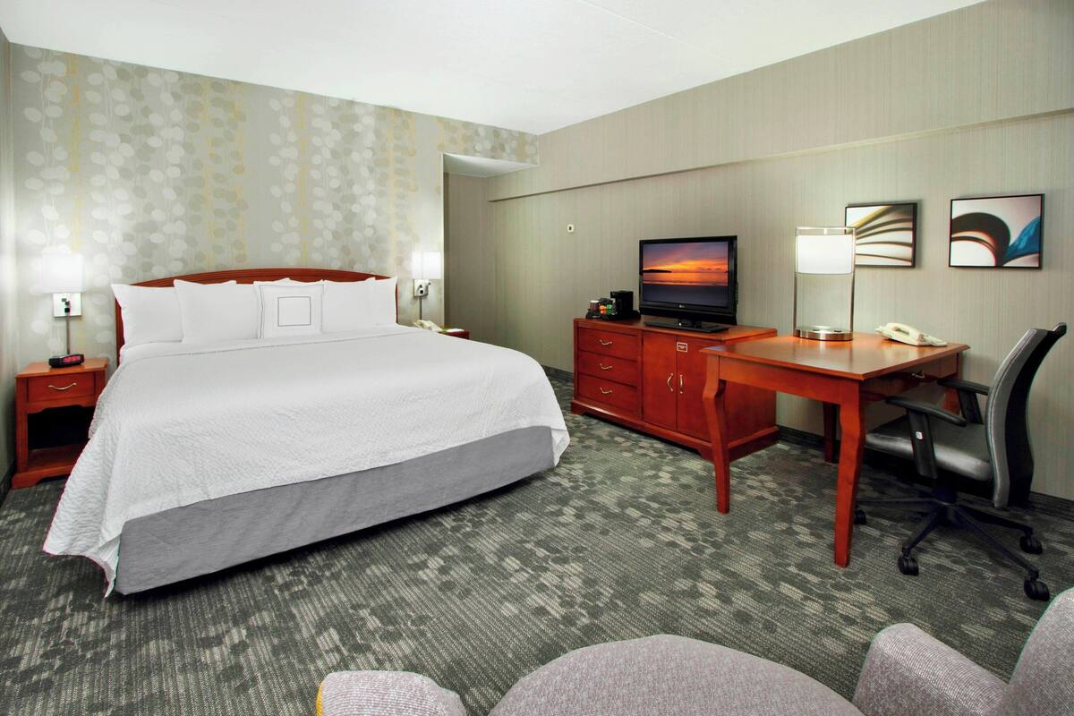 Habitación de hotel con una cama grande, un escritorio con computadora, televisor y una silla.