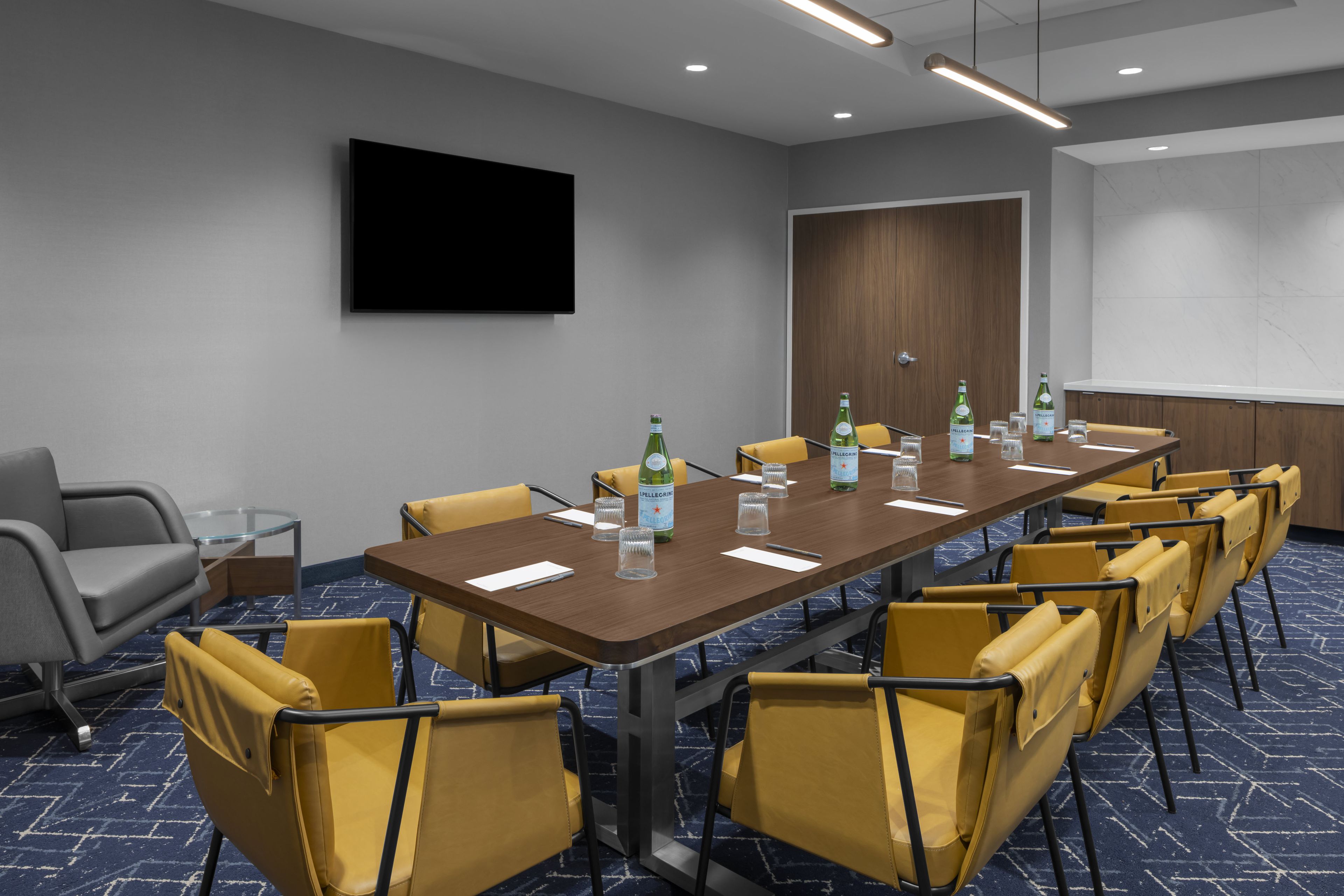 Un salón de conferencias con una mesa larga, sillas amarillas, un televisor de pantalla plana y una minibar.