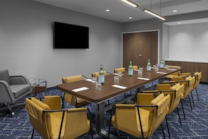 Un salón de conferencias con una mesa larga, sillas amarillas, un televisor de pantalla plana y una minibar.