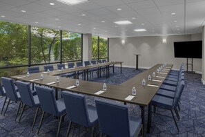 Ein Konferenzraum mit langen Tischen, Stühlen und einer Projektionsleinwand.