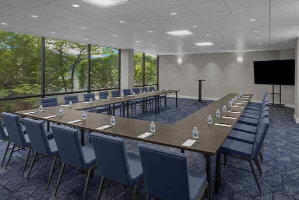 Een vergaderzaal met lange tafels, stoelen en een scherm voor een beamer.