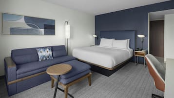 A hotel room with a bed, a sofa, a small table, and a lamp.