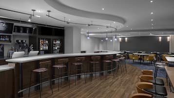 Uma área de bar moderna com balcão curvo, vários bancos e uma variedade de garrafas e copos.