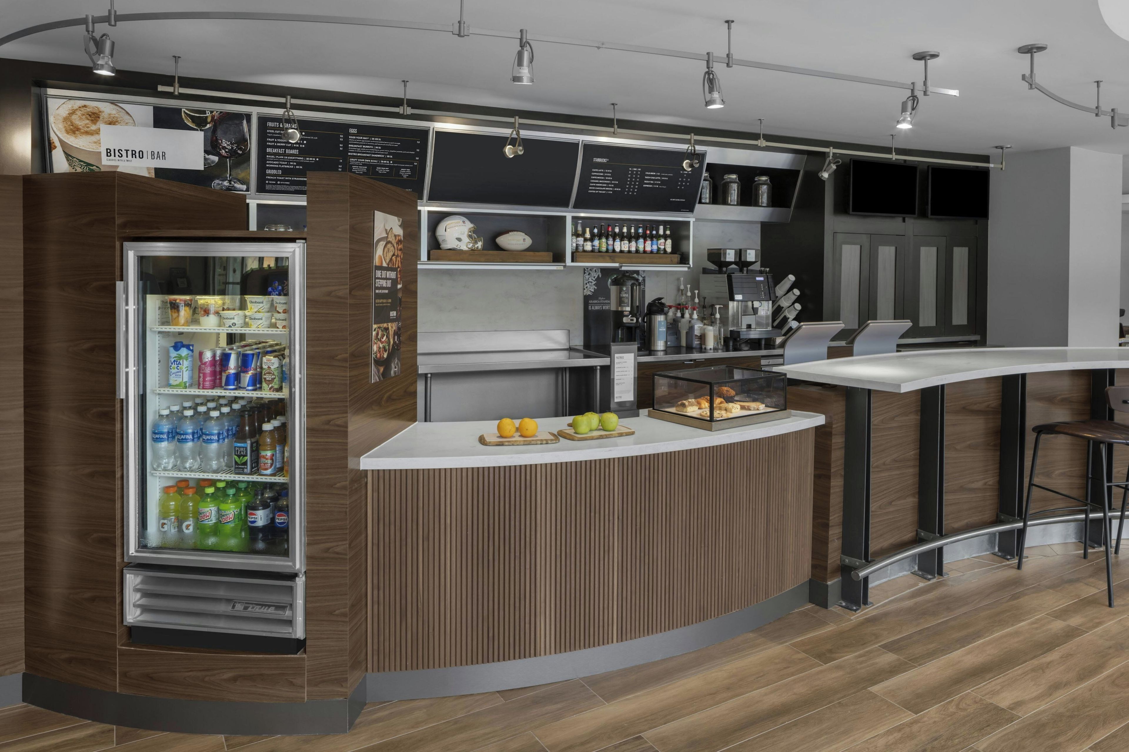 A modern bar area with a refrigerated display, a menu board, and a counter with bar tools.