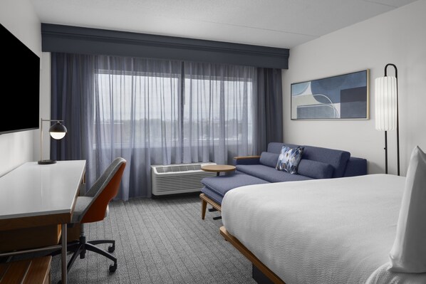 Une chambre d’hôtel comprenant un lit, un canapé, un bureau, une chaise, une télévision, une fenêtre avec des rideaux et un tableau au mur.