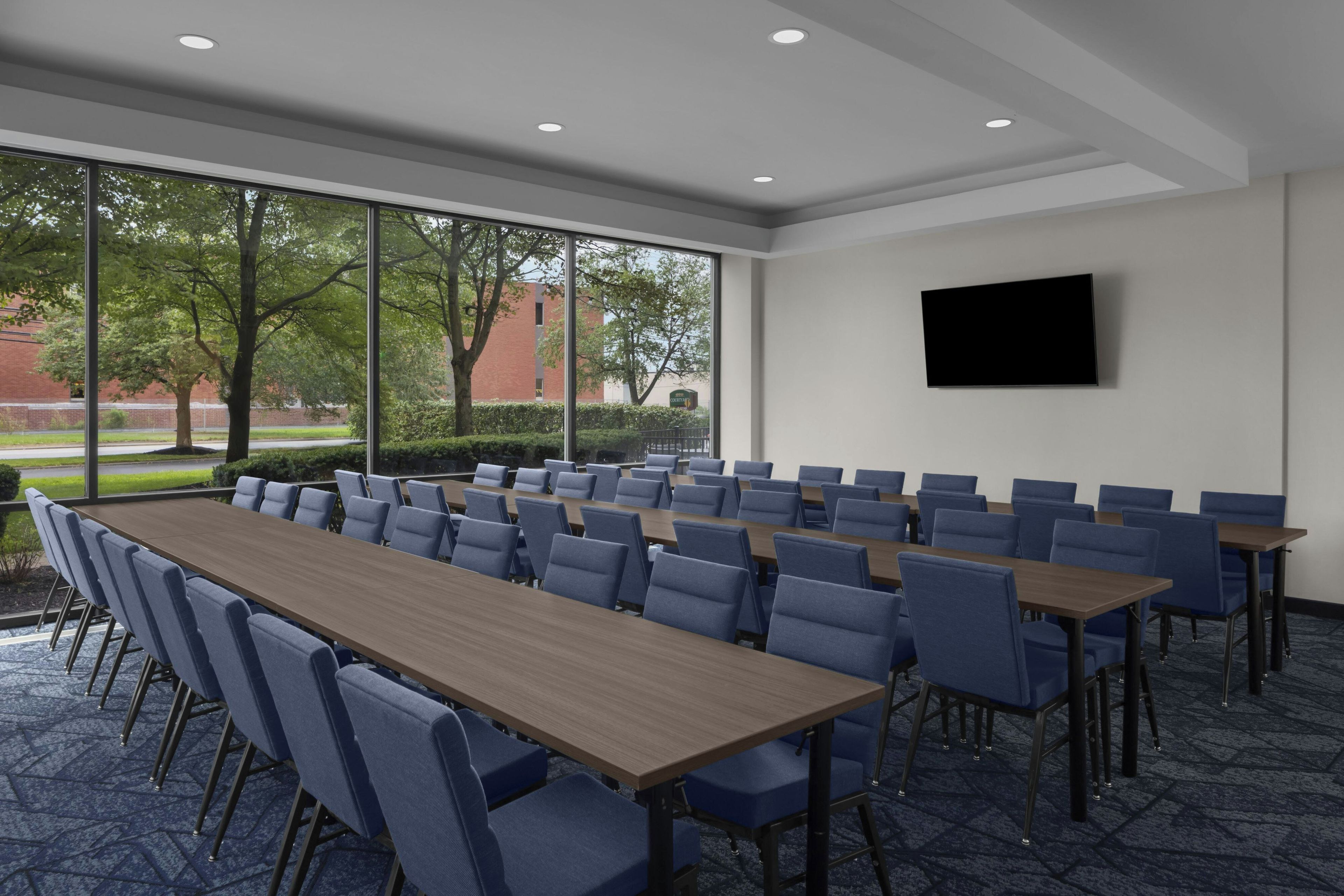 A conference room with a long table and chairs, large windows, and a flat-screen TV on the wall.
