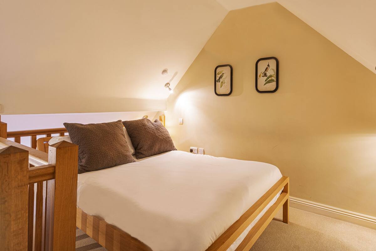 Een slaapkamer met een houten bed, twee kussens, een nachtkastje en een aan de muur hangend schilderij.