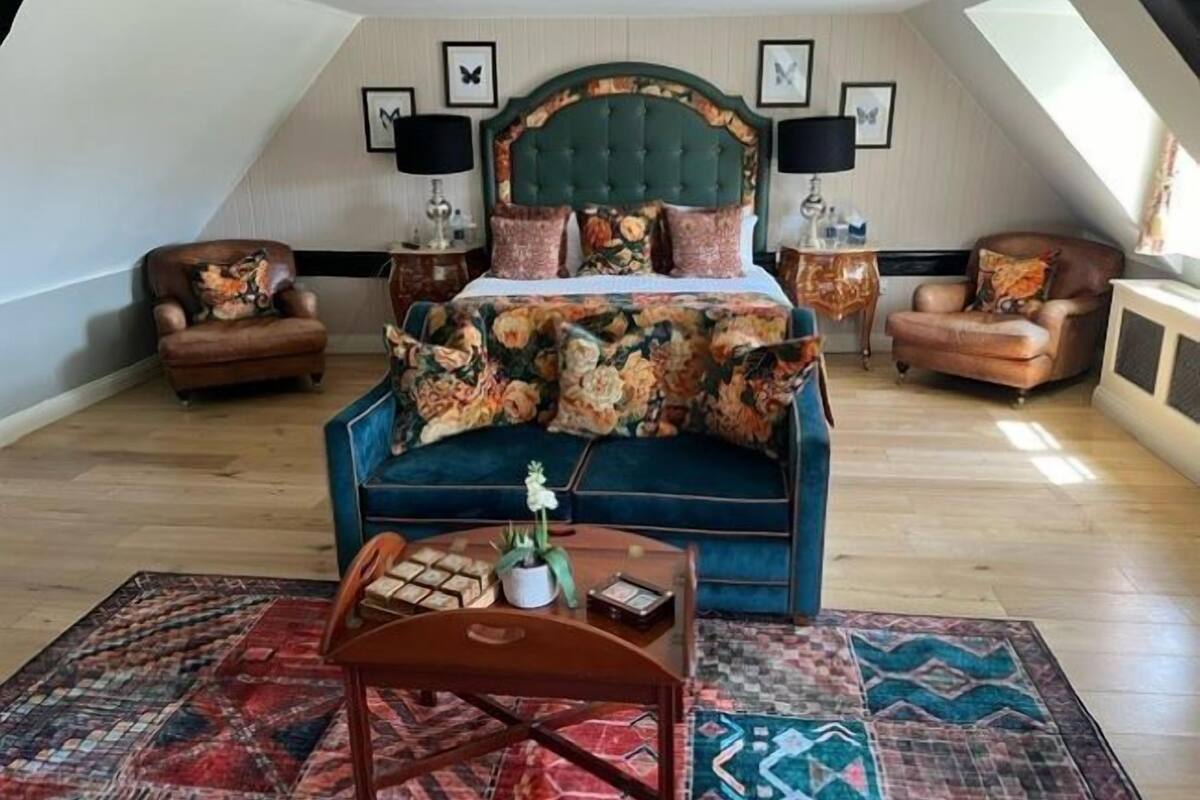 Een slaapkamer met een groot bed, twee fauteuils, een bijzettafeltje en een kamerbreed tapijt.