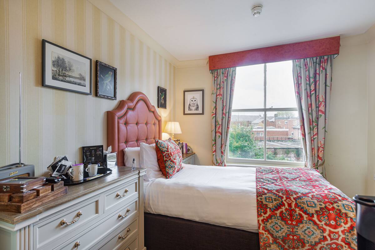 Een hotelkamer met een bed, een kaptafel, een nachtkastje, een lamp en ingelijste foto's aan de muur.