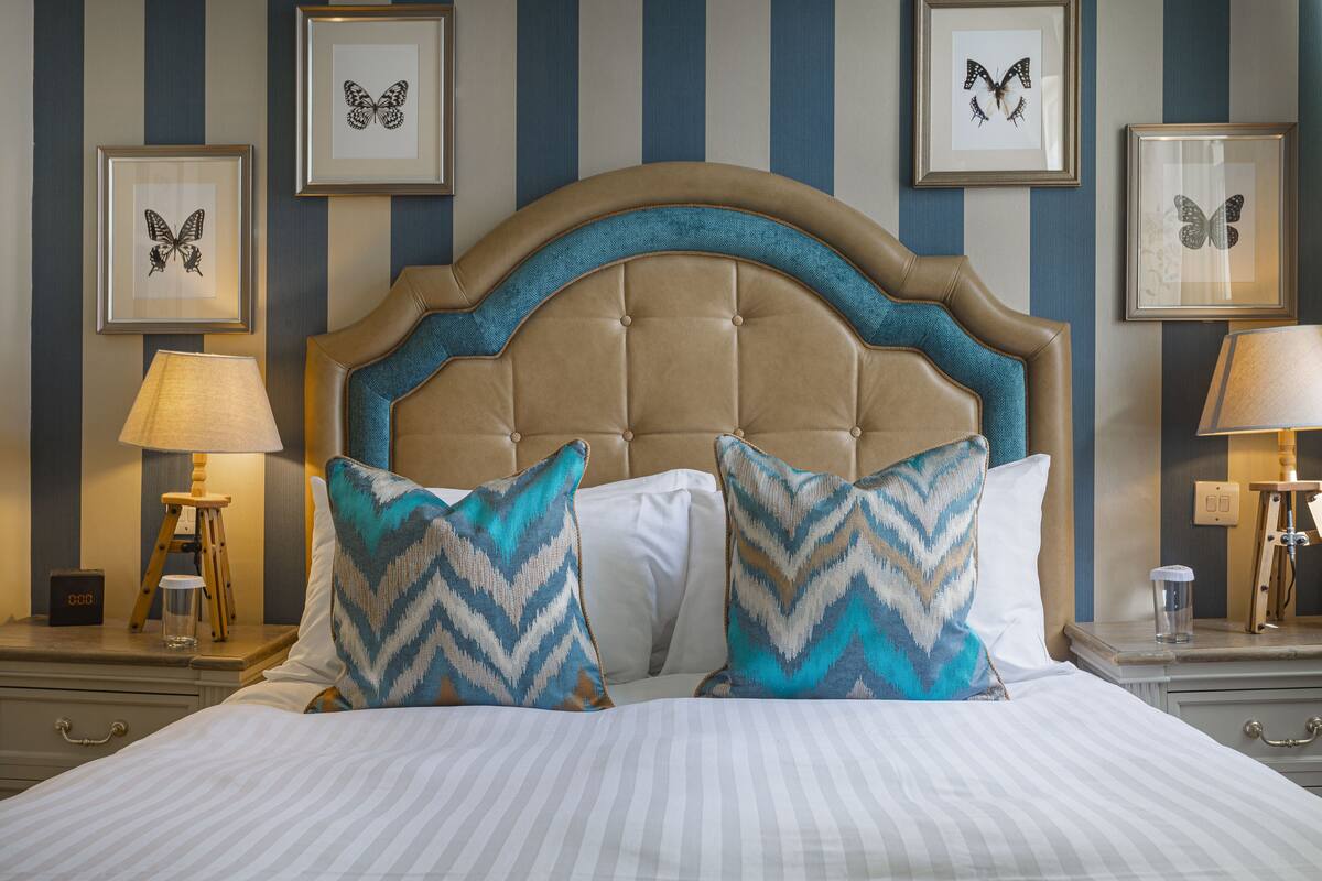 Een netjes opgemaakt bed met gestreepte lakens, een gebonden hoofdbord en decoratieve kussens.
