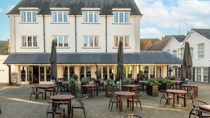 Ein zweistöckiges Gebäude mit einer Terrasse, die Sitzgelegenheiten und Pflanzgefäße im Freien bietet.