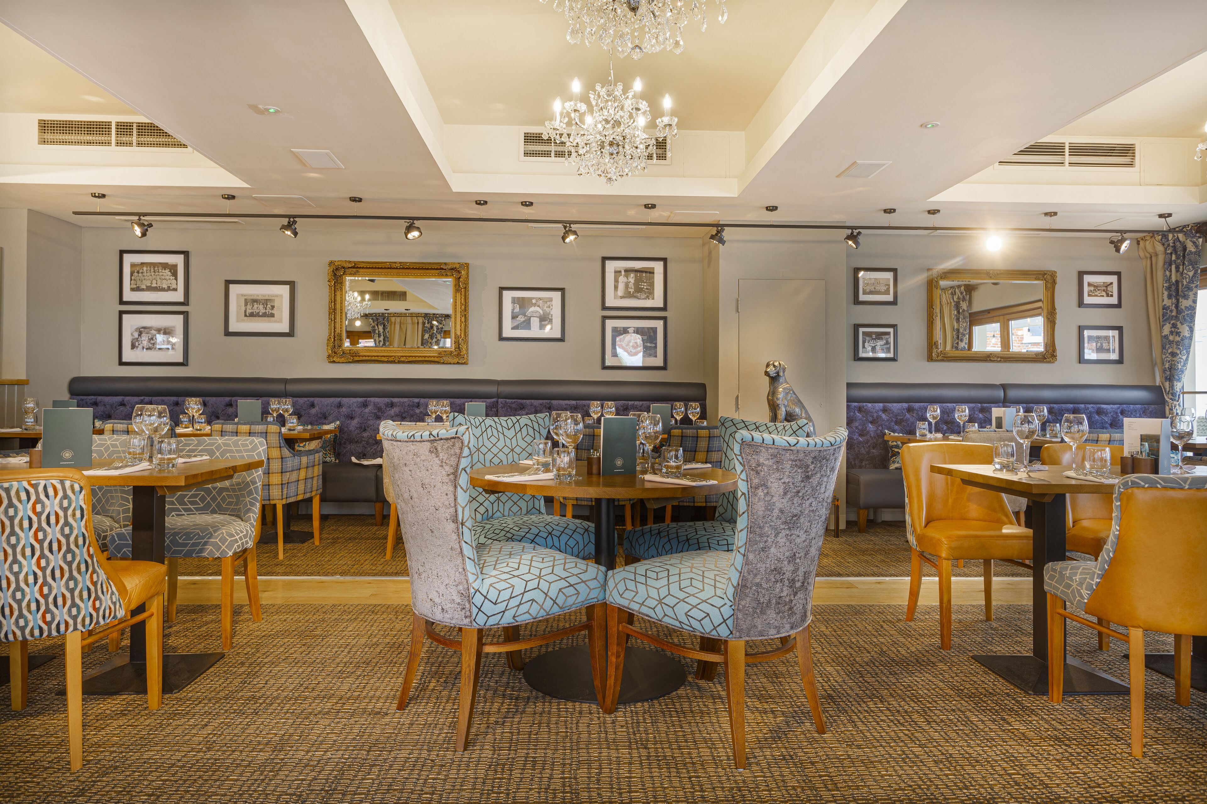 A restaurant with round tables, patterned chairs, and framed pictures on the walls.