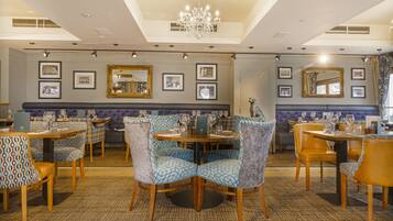 A restaurant with round tables, patterned chairs, and framed pictures on the walls.