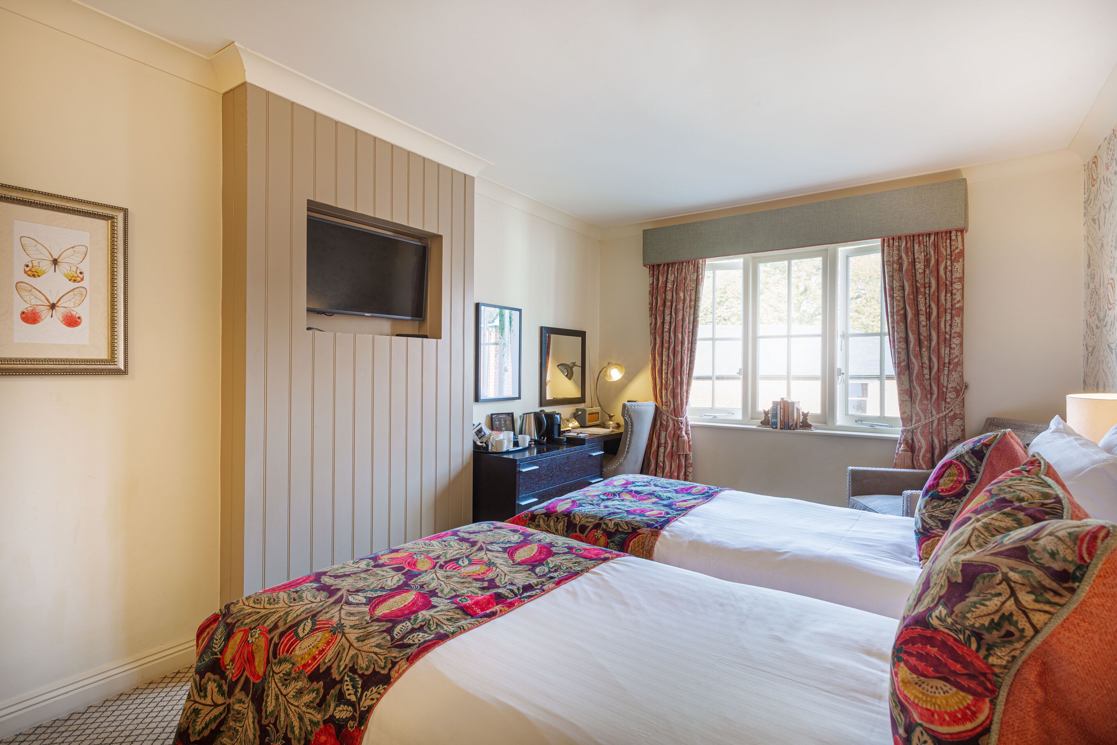 Une chambre d’hôtel avec deux lits, un bureau, une télévision et une fenêtre avec des rideaux.