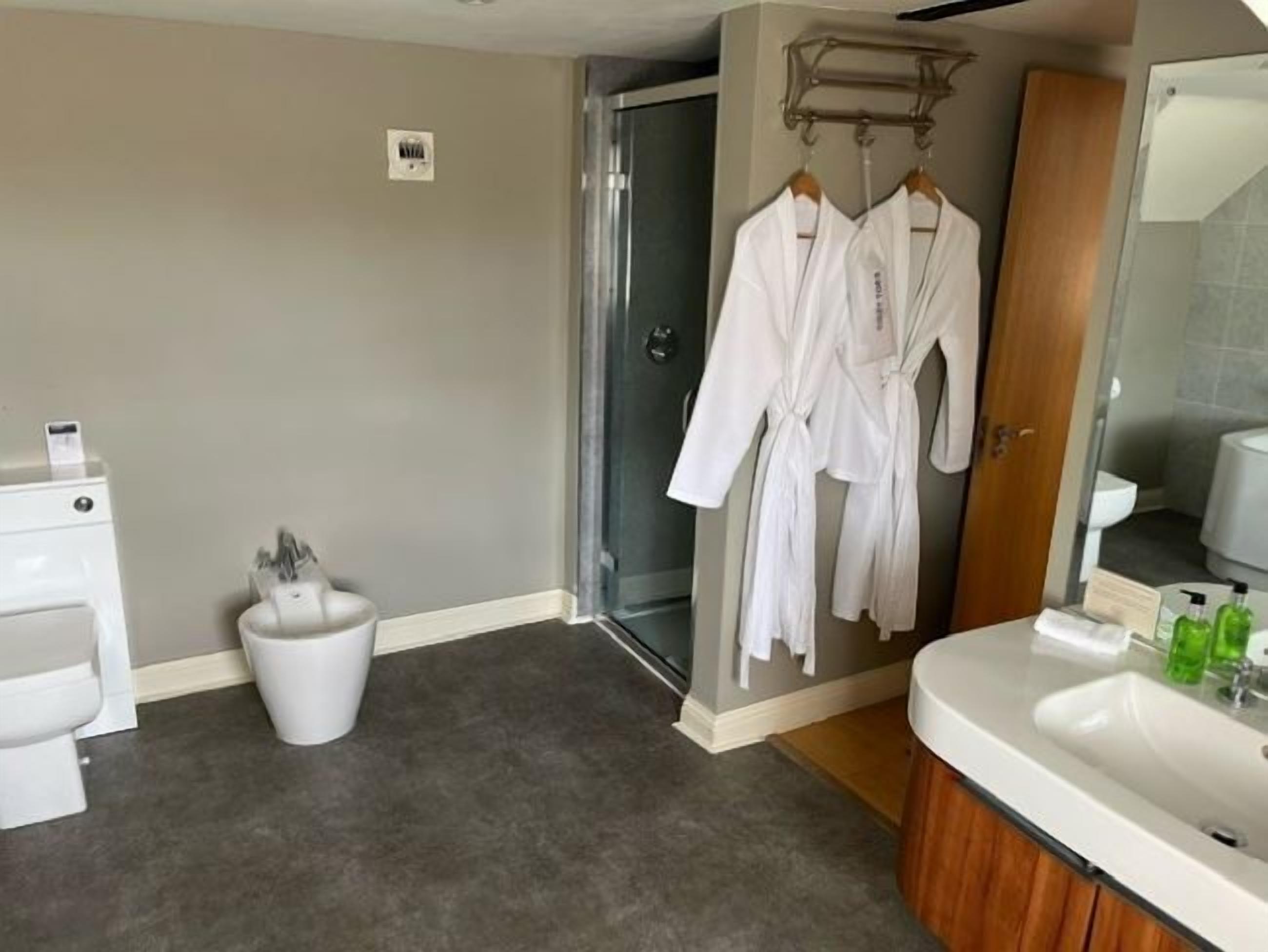 A bathroom with a shower, a sink, and a toilet. There are two white robes hanging on a rack.