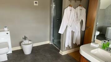 A bathroom with a shower, a sink, and a toilet. There are two white robes hanging on a rack.