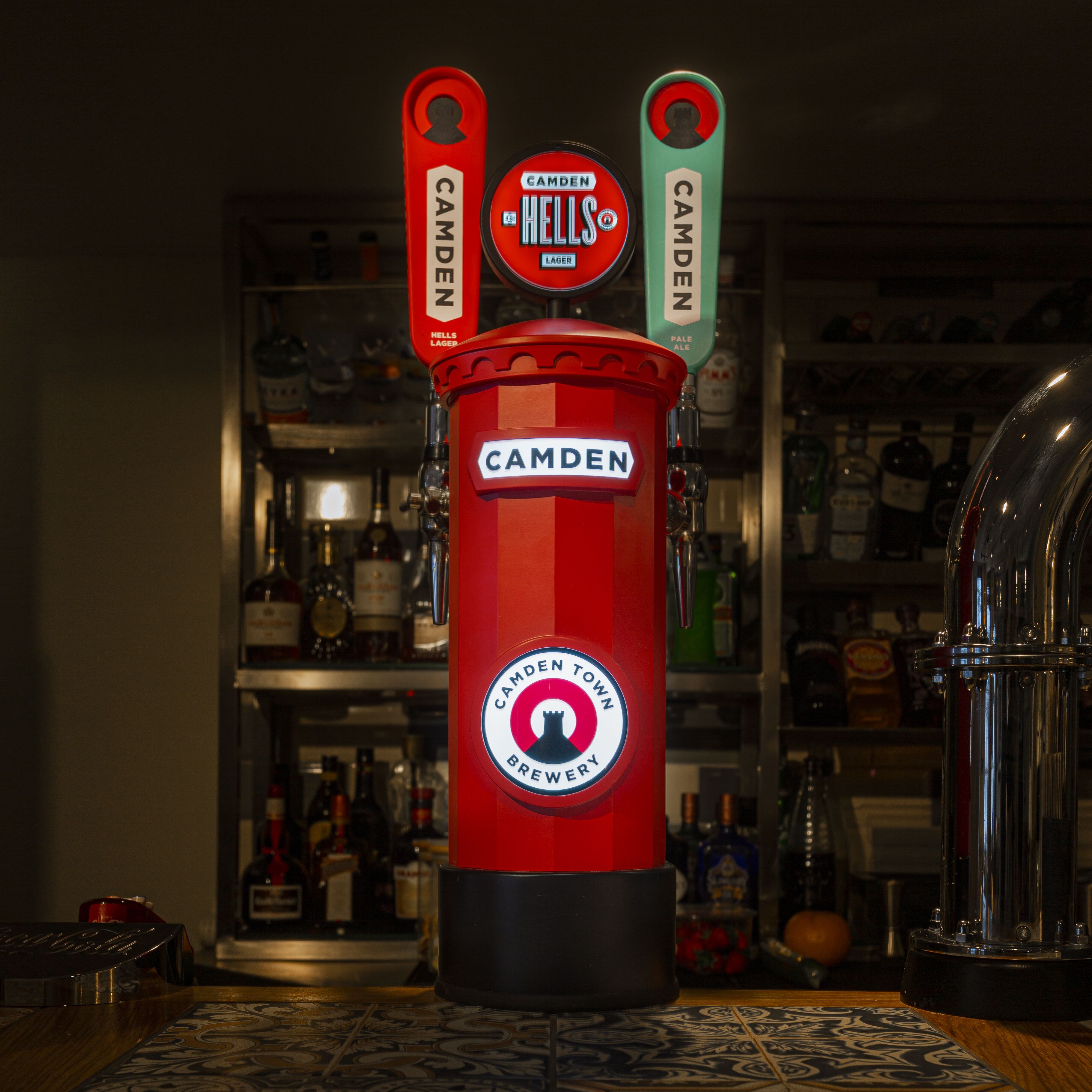 A red beer tap labeled "Camden Hells Lager" with a "Camden Town Brewery" logo.