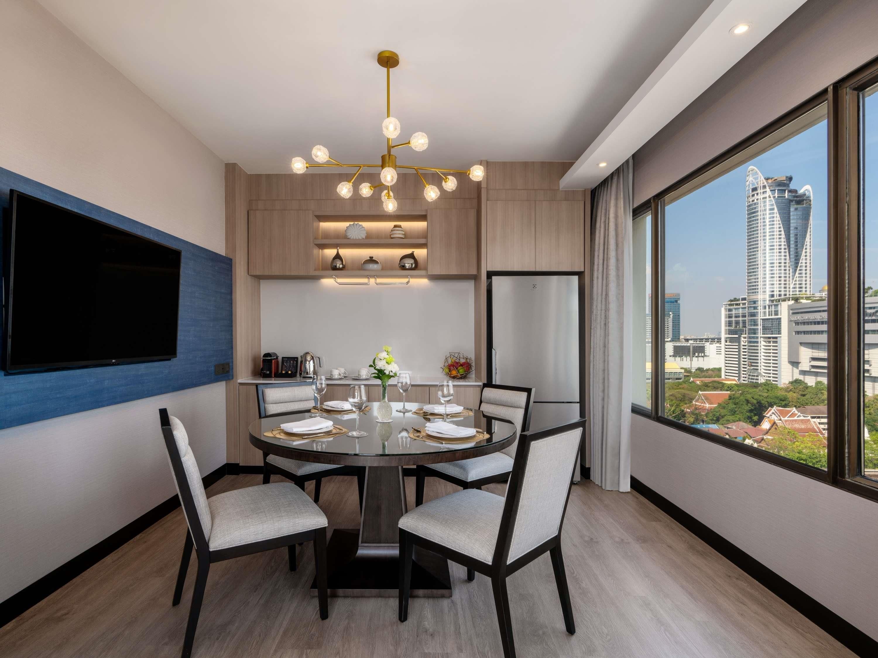 A modern dining area with a round table, chairs, a chandelier, a flat-screen TV, and a city view.