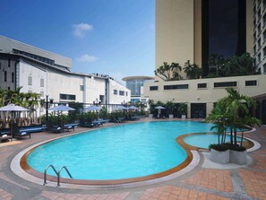 Relax by the inviting pool surrounded by lounge chairs and umbrellas, set amidst lush greenery and a unique blend of modern and traditional architecture.