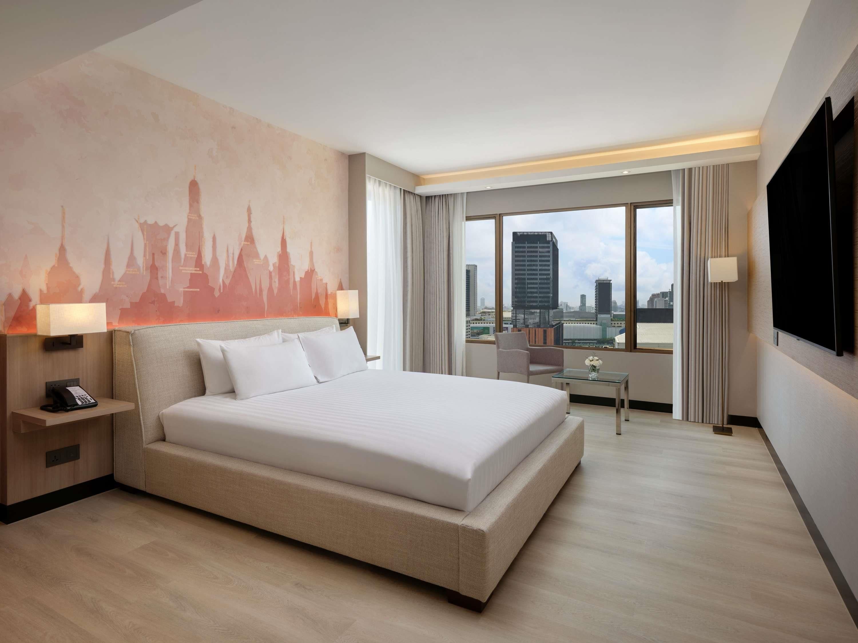Une chambre d’hôtel avec un grand lit, un bureau, une chaise, une télévision et une vue sur la ville.