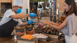 A chef preparing food in a kitchen with a customer receiving a dish. - Novotel Bangkok On Siam Square (Bangkok)