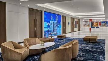 A modern hotel lobby with a large digital screen displaying a cityscape, comfortable seating, and a clean, well-lit interior.