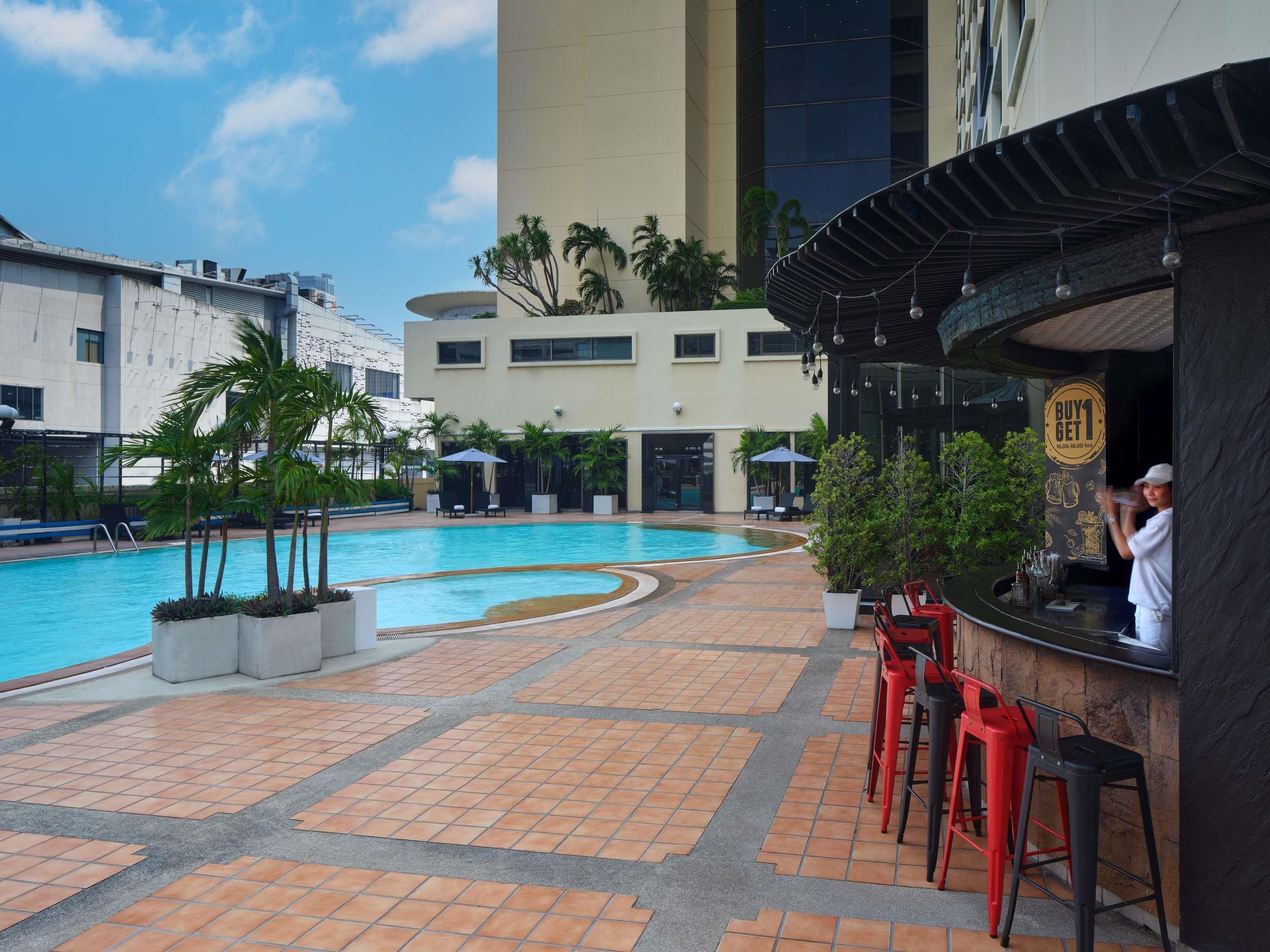 A swimming pool area with a bar and seating, surrounded by buildings.