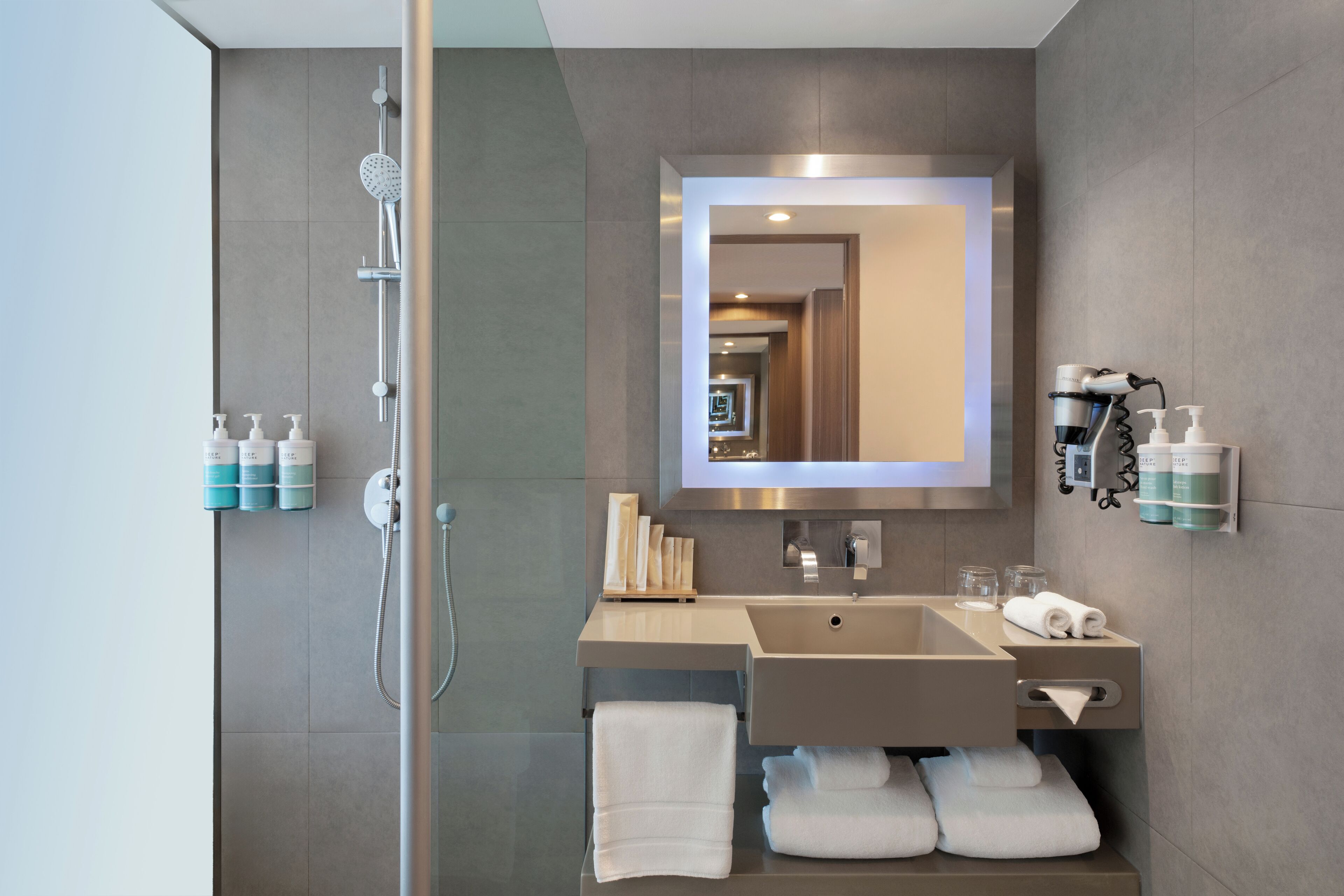 A modern bathroom with a glass-enclosed shower, a sink with a mirror above it, and toiletries on the wall.