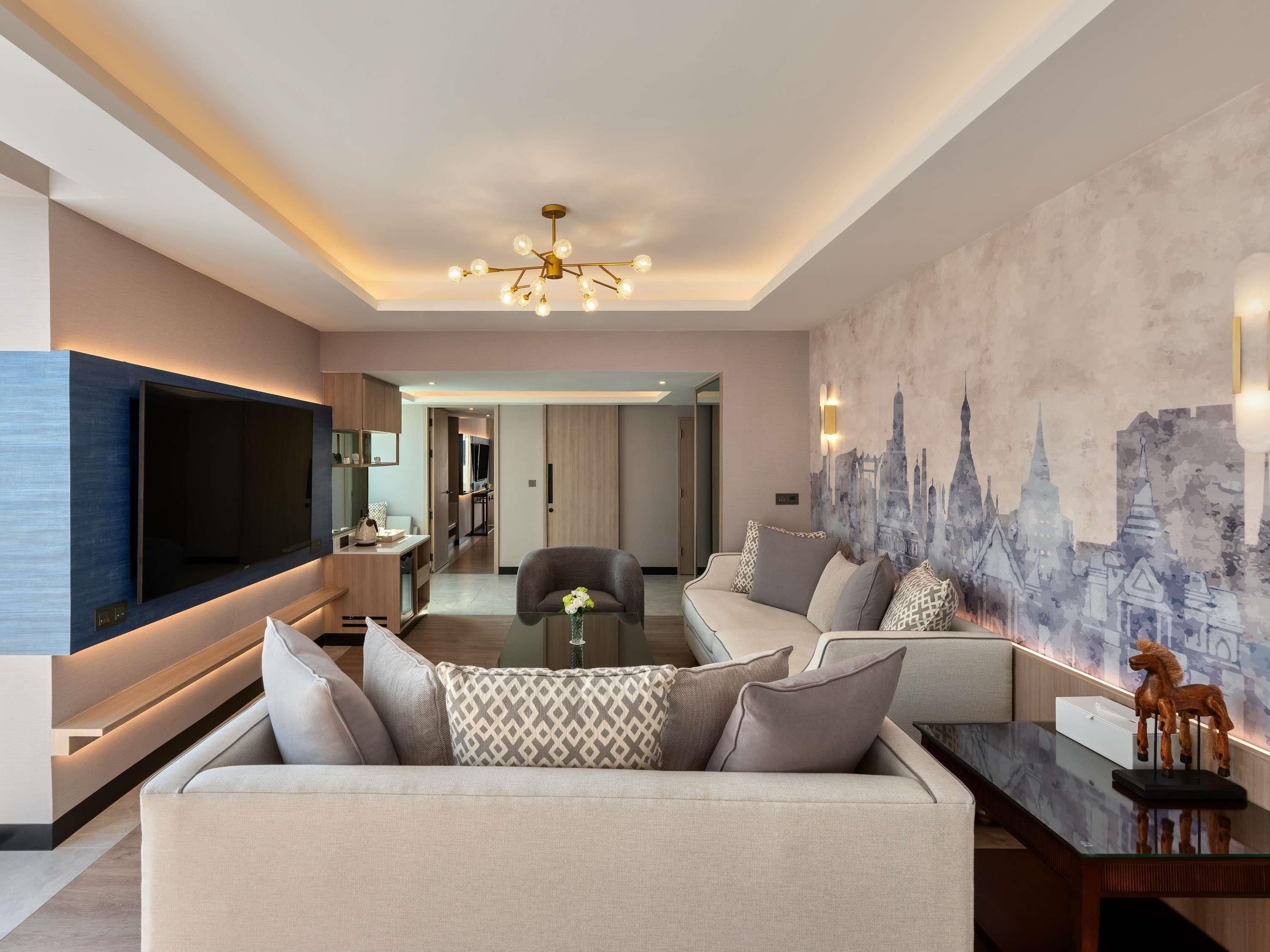 A modern living room with a flat-screen TV, a sofa with patterned cushions, a glass coffee table, and a cityscape mural on the wall.