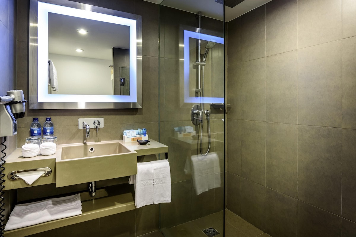 Ein modernes Badezimmer mit großem Spiegel, Waschbecken, Duschkabine aus Glas und Handtuchhalter.