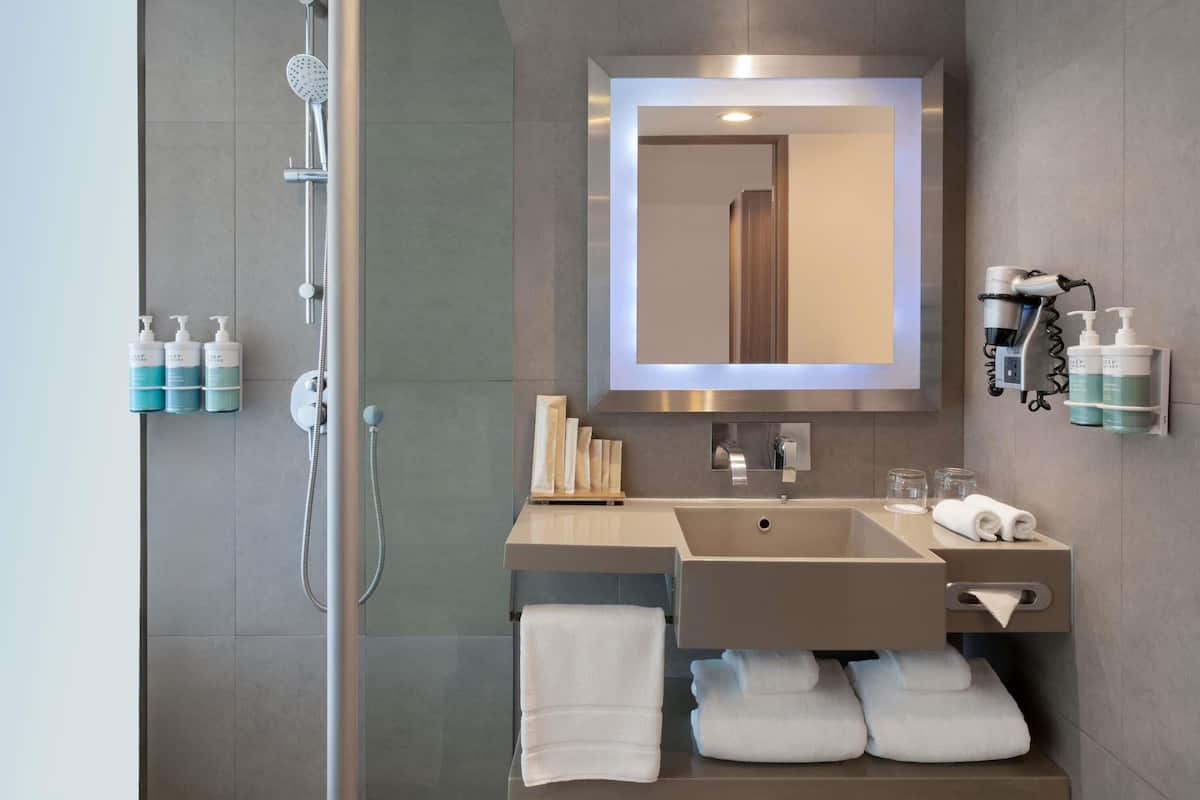 A modern bathroom with a shower, a sink, a mirror, and toiletries.