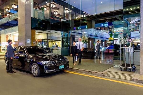 A modern hotel lobby with a black car parked outside, glass walls, and a reception desk. - Novotel Bangkok On Siam Square (Bangkok)