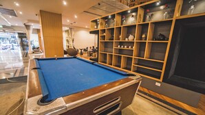 Una mesa de billar en una habitación bien iluminada con un mueble de madera que exhibe diversos objetos decorativos.