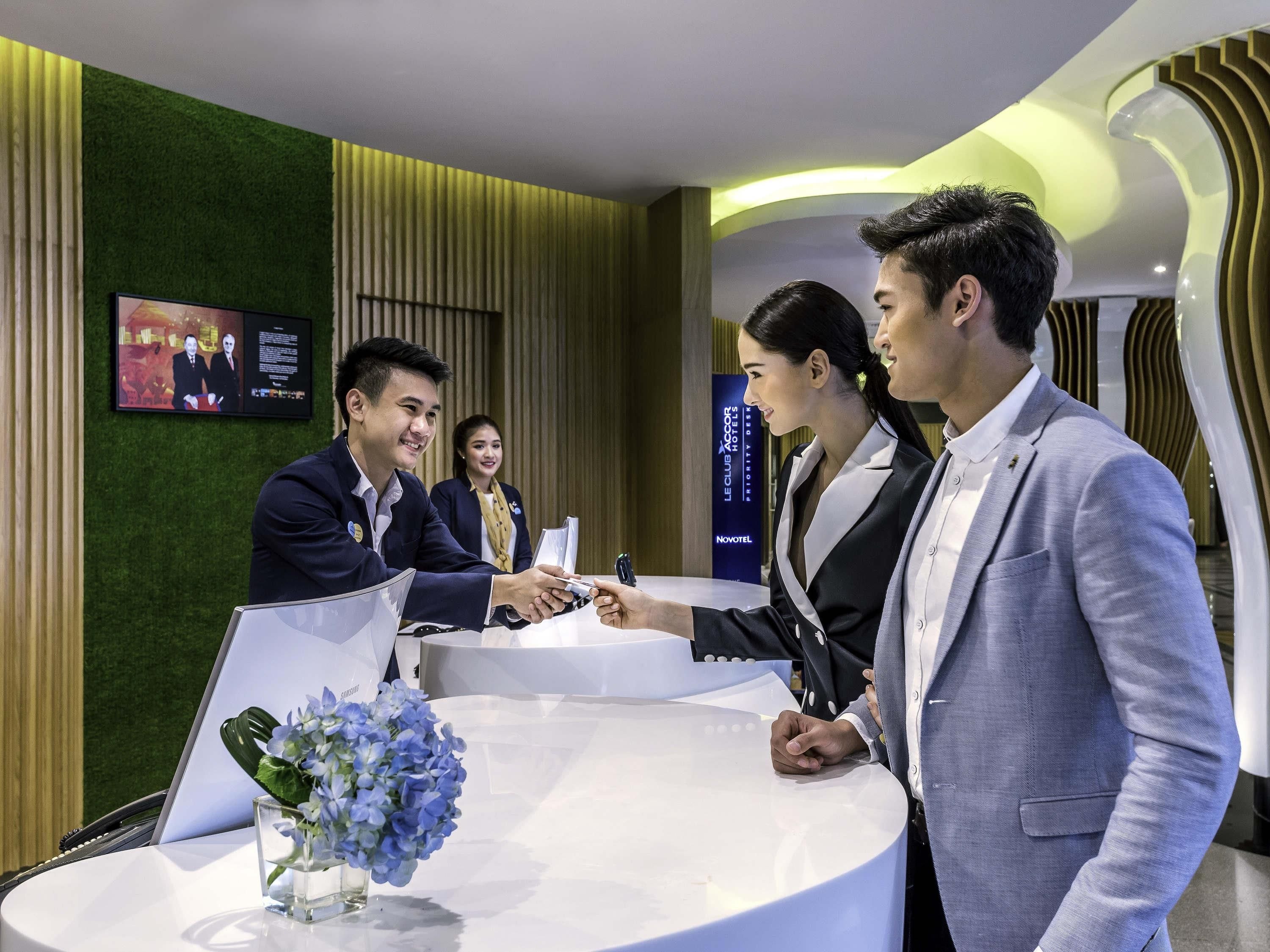A reception desk with a Samsung device, a glass vase with flowers, and a Novotel sign.