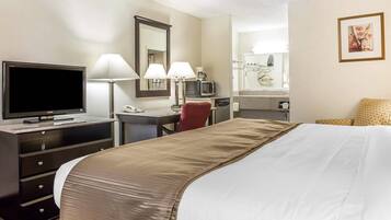 A hotel room with a bed, a desk with a TV, two lamps, a chair, a mirror, and a picture on the wall.