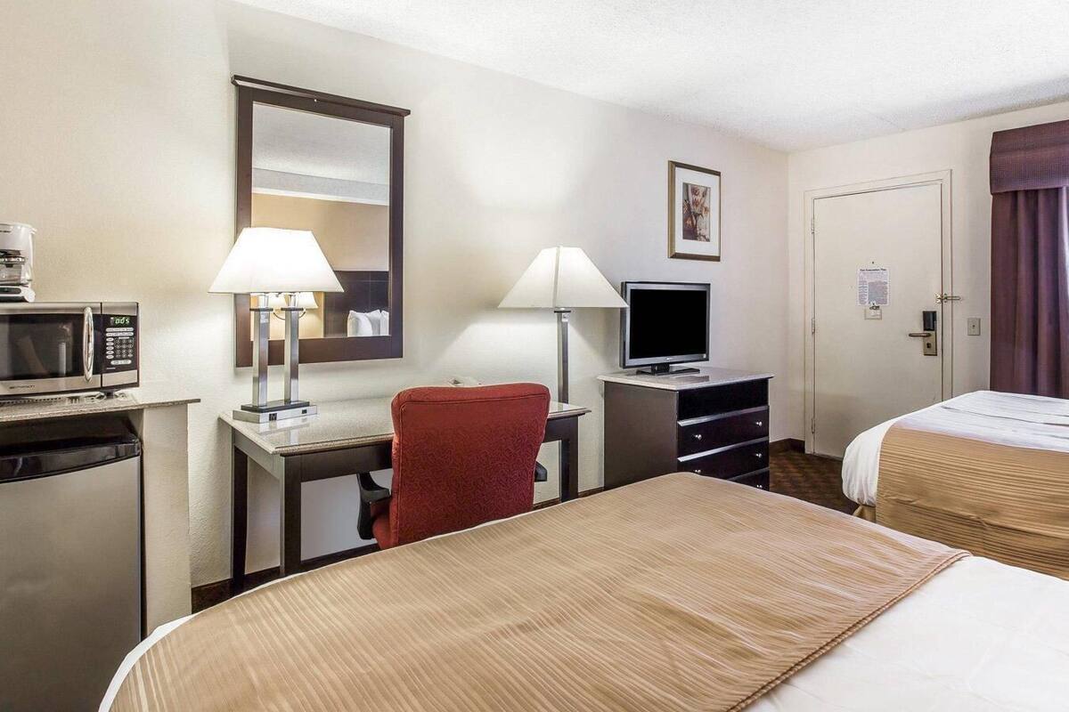 A hotel room with a bed, a desk with a computer, a microwave, a red chair, and a television.