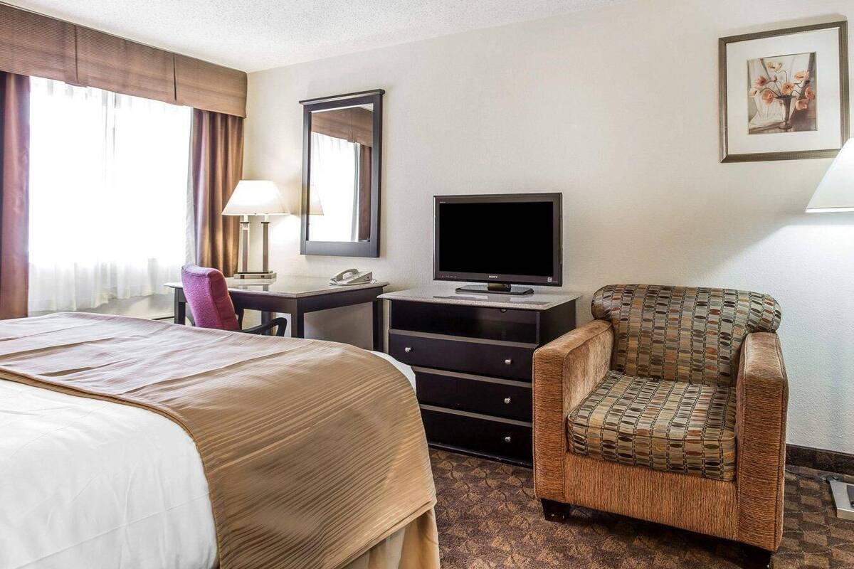 A hotel room with a bed, a desk with a computer and TV, a chair, and a framed picture on the wall.