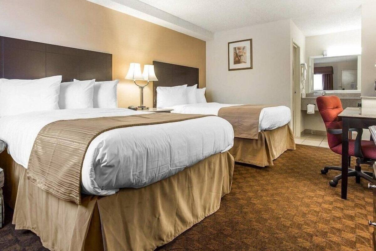 A hotel room with two beds, a desk, a chair, and a bathroom visible through an open door.